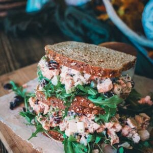 Leftover turkey salad sandwich with arugula and cranberries on whole grain bread, served on a wooden board with a rustic background.