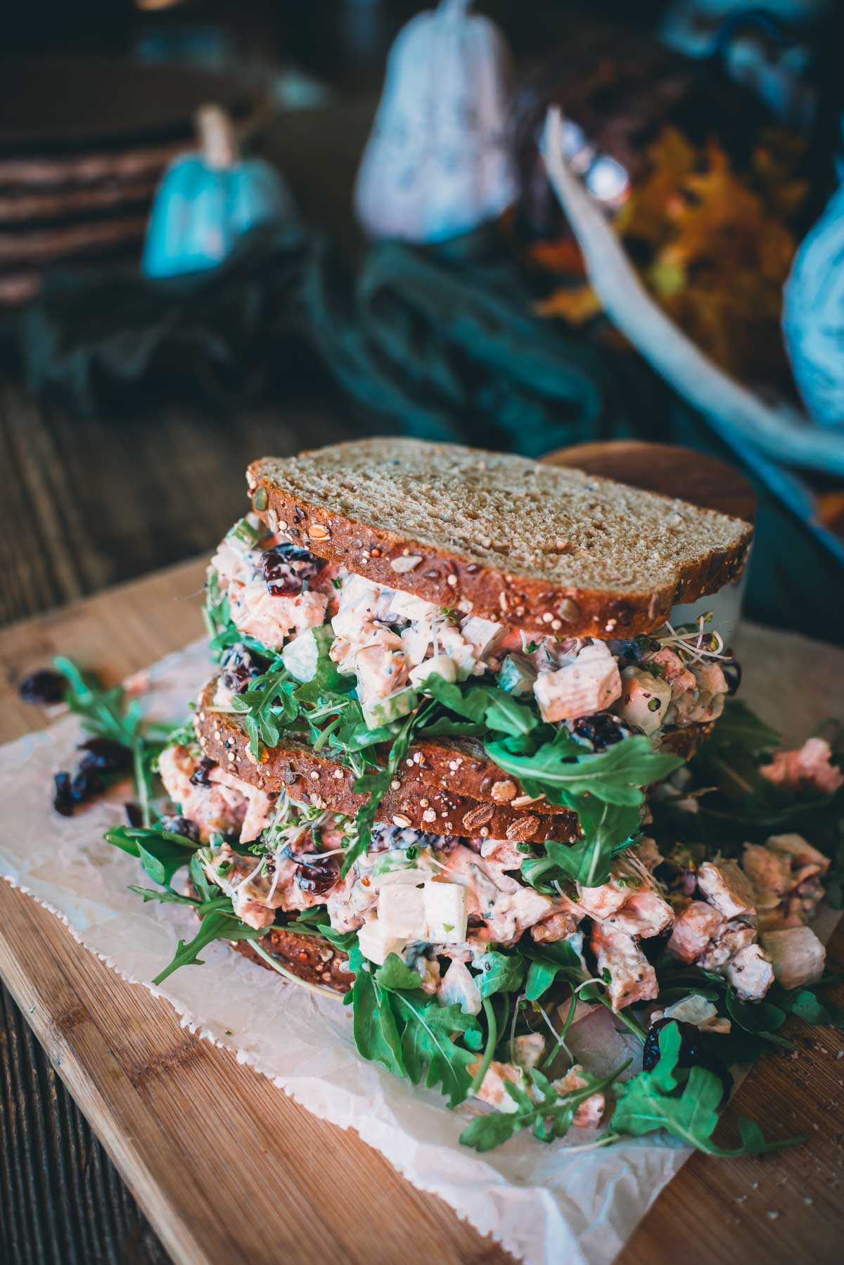 Leftover turkey salad sandwich with arugula and cranberries on whole grain bread, served on a wooden board with a rustic background.