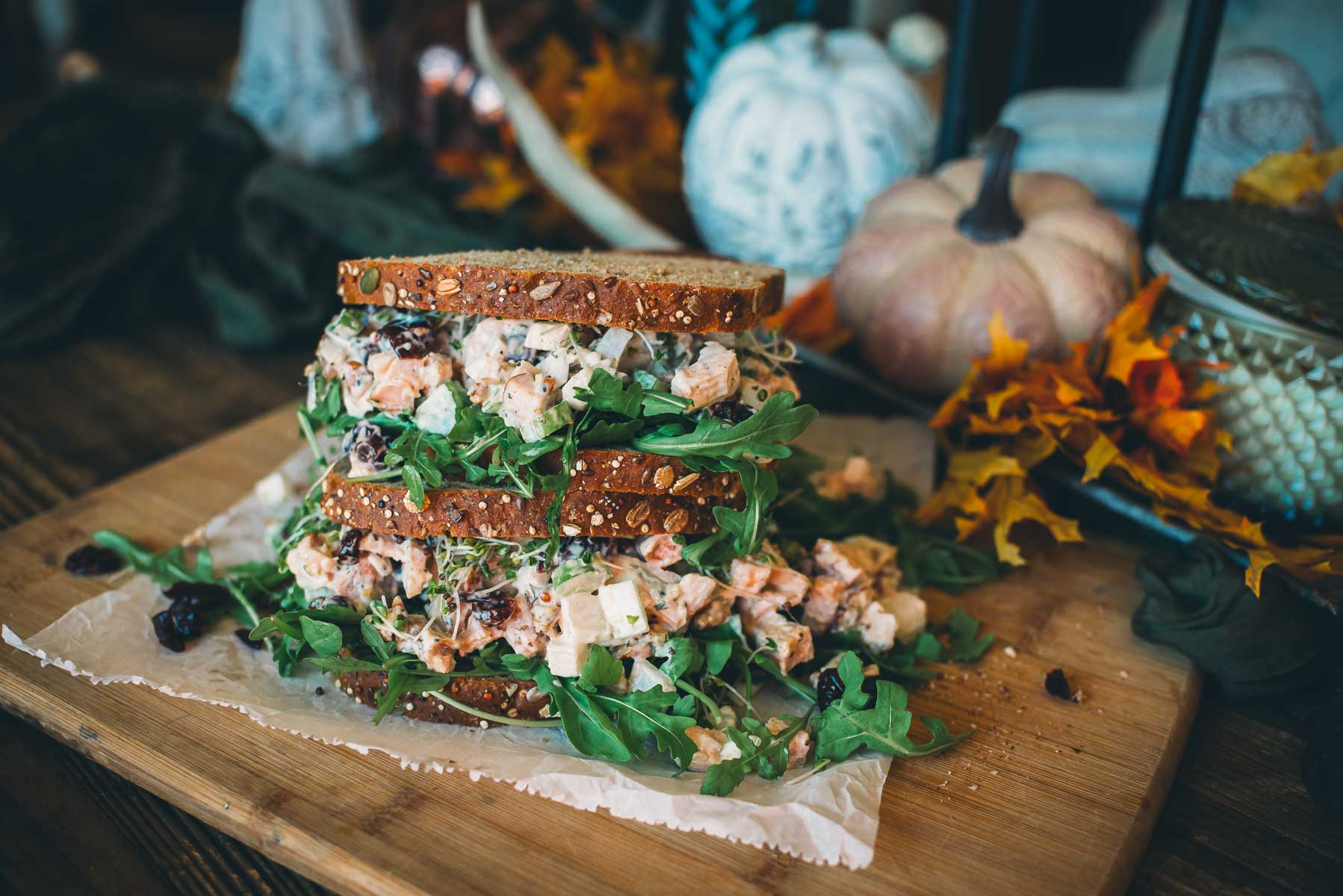 Two sandwiches with wheat bread, filled with turkey salad and arugula, are stacked on parchment paper.