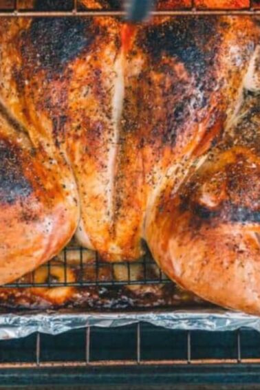 A spatchcocked turkey, seasoned and roasted, on a wire rack over a foil-lined baking sheet in an oven.