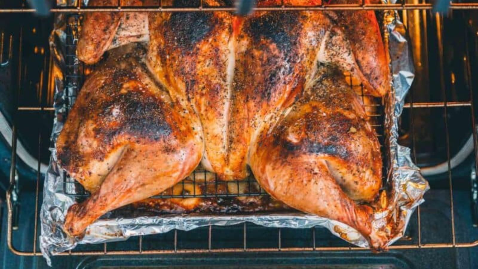 A spatchcocked chicken, seasoned and roasted, on a wire rack over a foil-lined baking sheet in an oven.