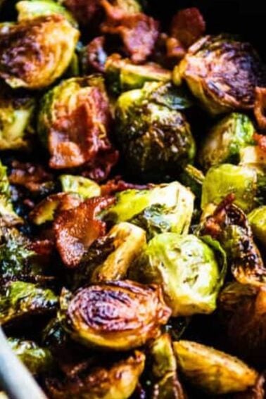 A cast iron skillet with roasted Brussels sprouts and crispy bacon, accompanied by a wooden spoon.