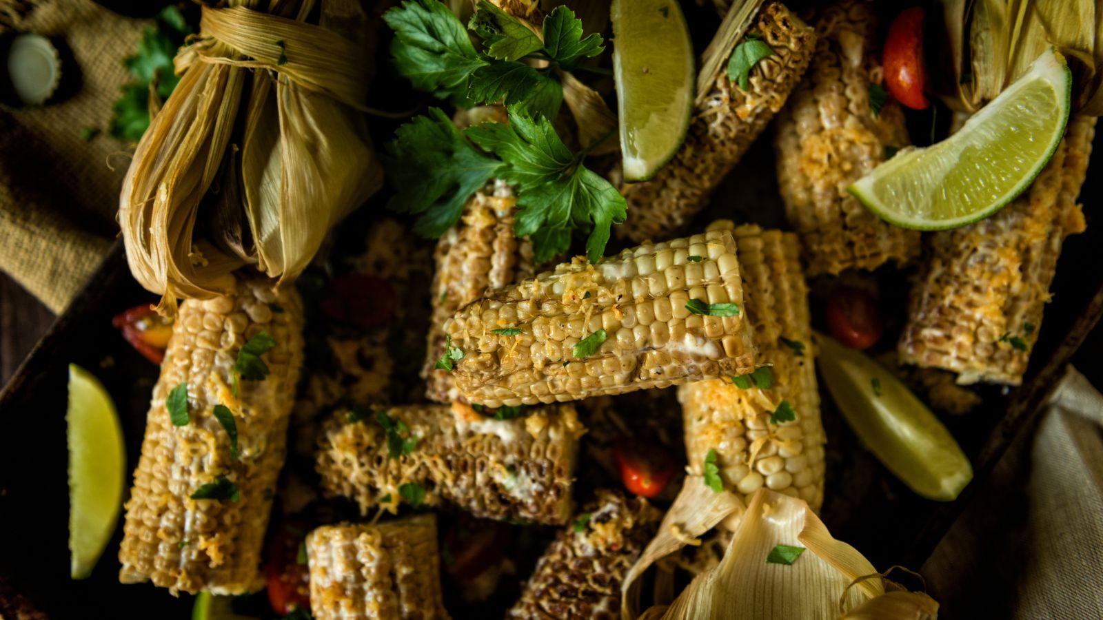 Grilled corn pieces garnished with herbs and lime wedges on a tray.