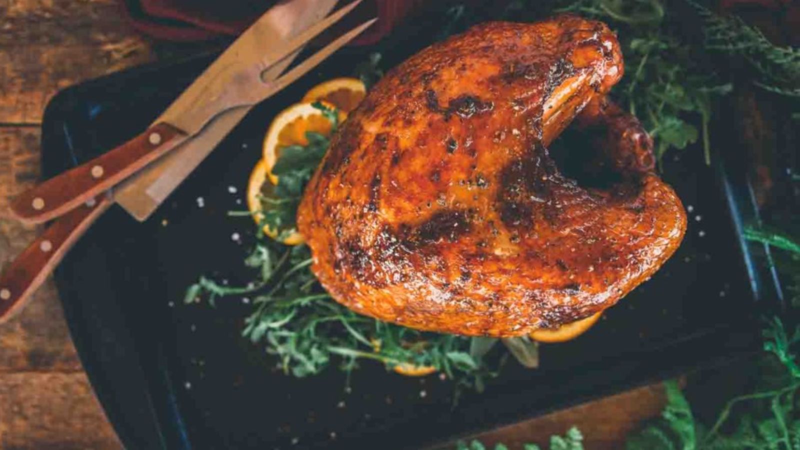 A roasted turkey breast on a black tray, garnished with sliced oranges and fresh herbs.