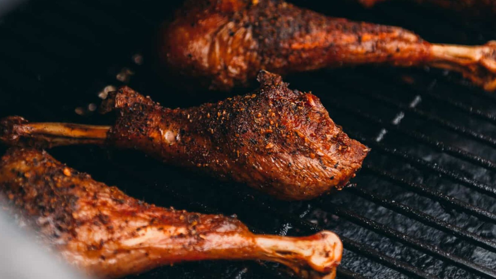 Grilled, seasoned turkey legs are shown on a grill surface, displaying a crispy and browned exterior.