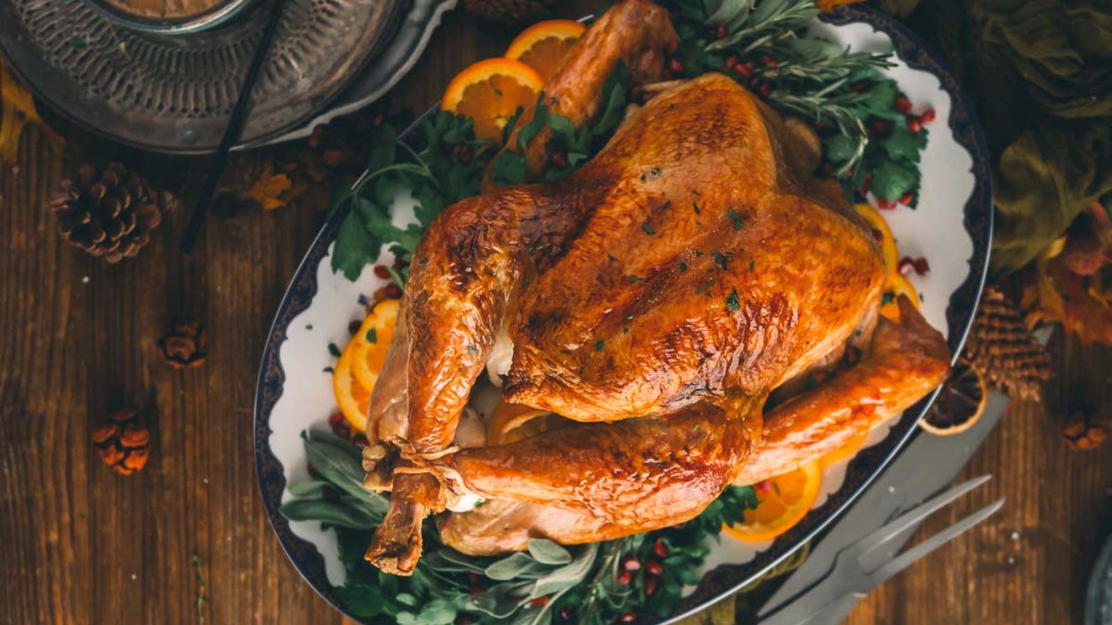 Roasted turkey on a platter, garnished with orange slices, herbs, and pomegranates, placed on a wooden table.