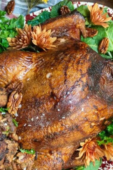 Roasted turkey with stuffing on a platter, garnished with herbs and nuts. Surrounded by a checkered cloth and autumn decorations.