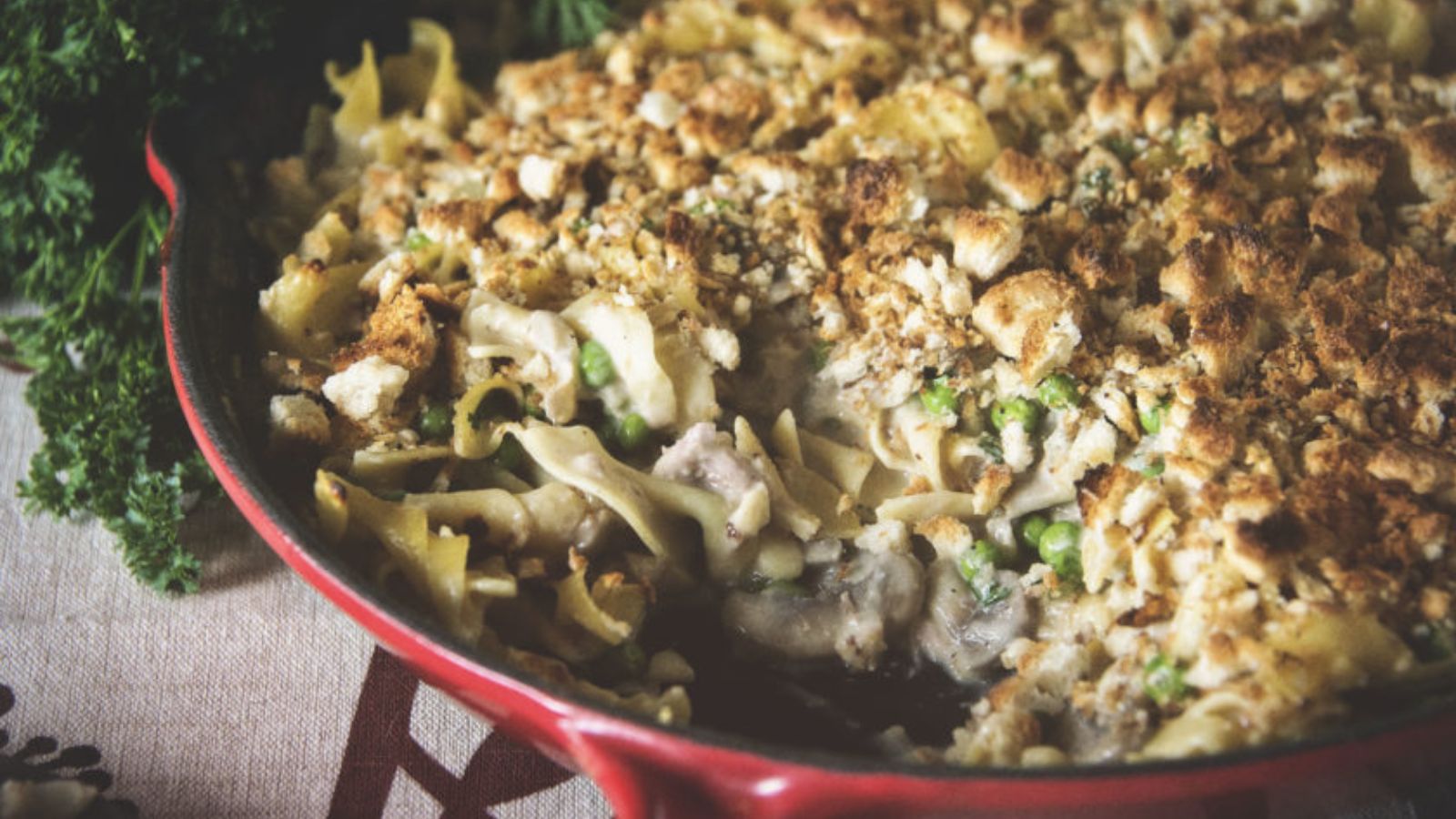 A casserole dish filled with creamy pasta, peas, and chicken, topped with a layer of browned breadcrumbs.