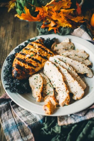 Grilled turkey tenderloin and sliced turkey on a white plate, garnished with herbs and surrounded by kale, with autumn leaves in the background.