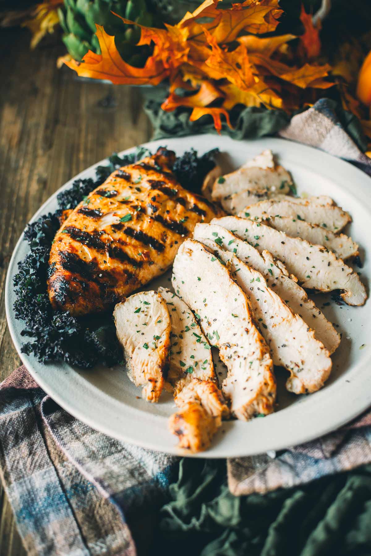 Grilled turkey tenderloin and sliced turkey on a white plate, garnished with herbs and surrounded by kale, with autumn leaves in the background.