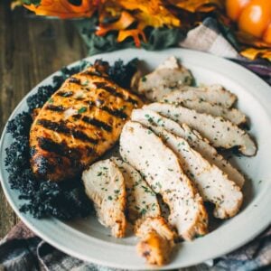 Grilled and sliced turkey tenderloin on a plate garnished with kale, surrounded by fall-themed decor and a small pumpkin.