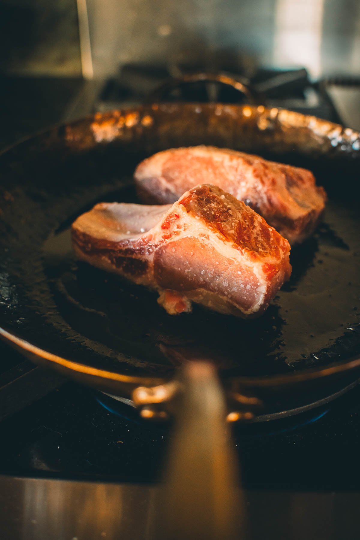 Two boar chops in a frying pan on a stove.