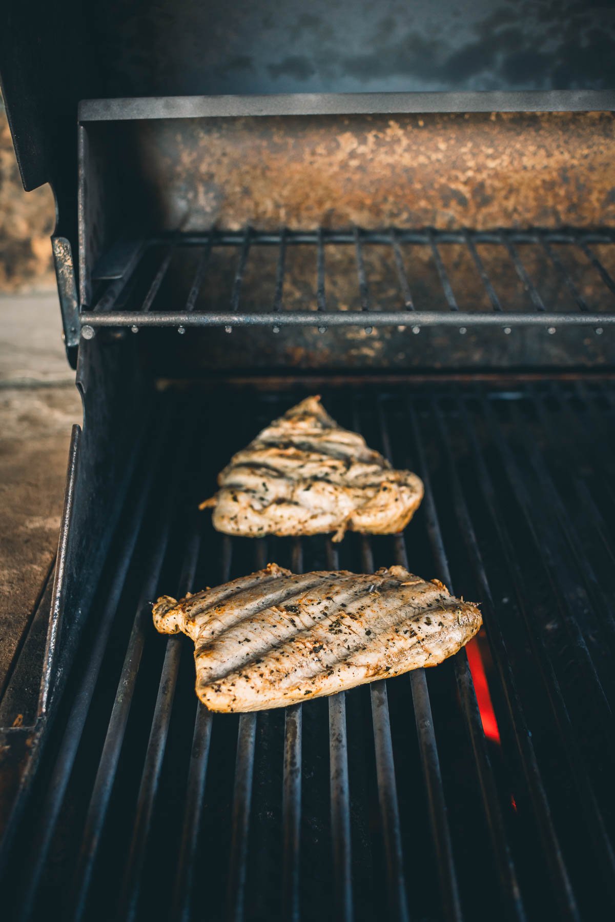 Two seasoned turkey tenderloin breasts grilling on an open flame barbecue.