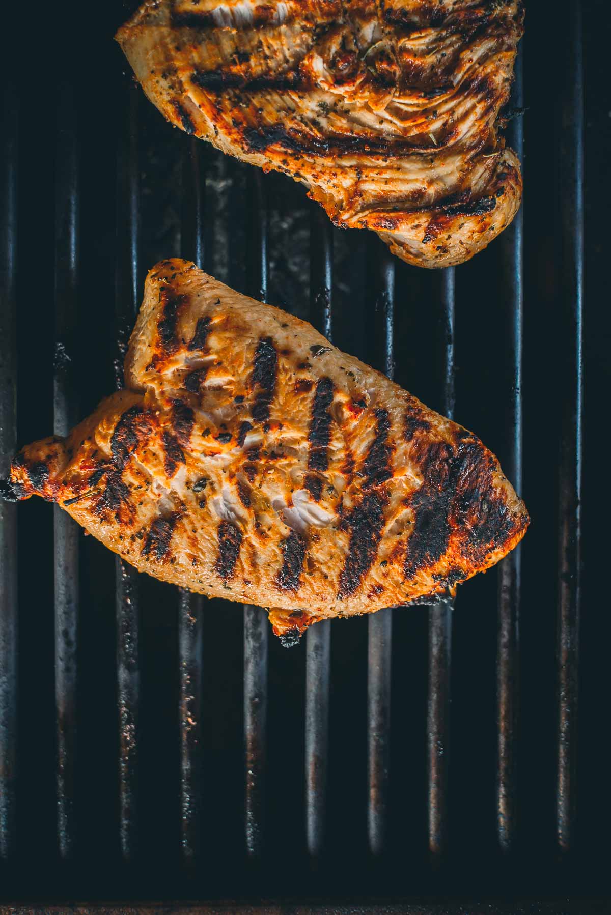 Two pieces of grilled turkey tenderloins with char marks on a black grill.