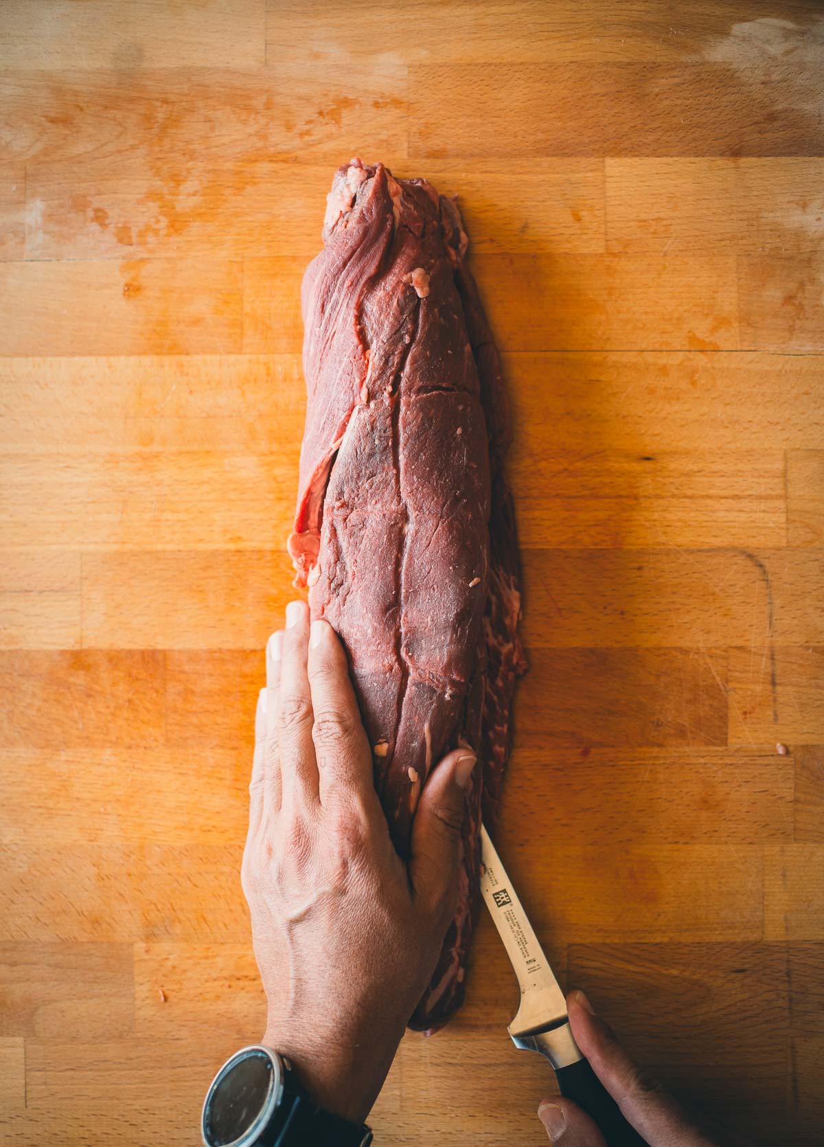 Person slicing a large beef tenderloin on a wooden cutting board.