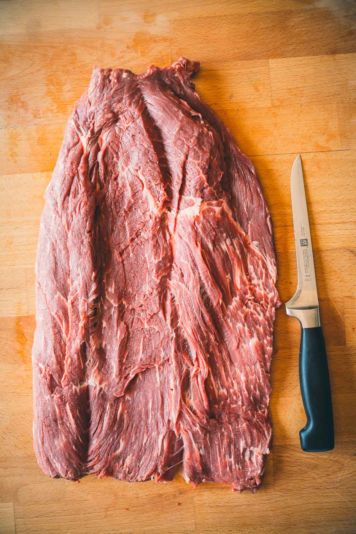 A large piece of raw beef tenderloin butterflied open on a wooden cutting board next to a chef's knife.