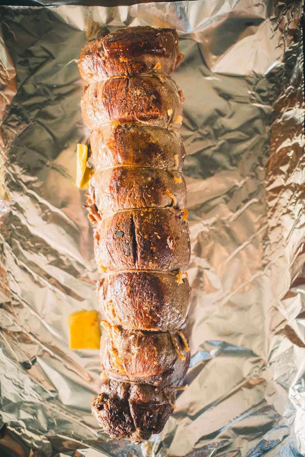 Rolled and tied stuffed beef tenderloin on foil, seasoned and cooked, with visible sear.