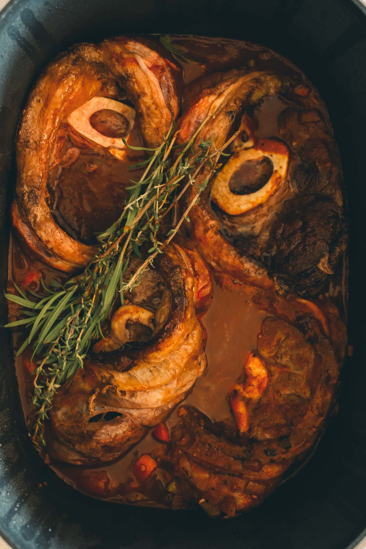 A pot of slow cooker beef shanks with bones, topped with fresh herbs, in a rich brown sauce.