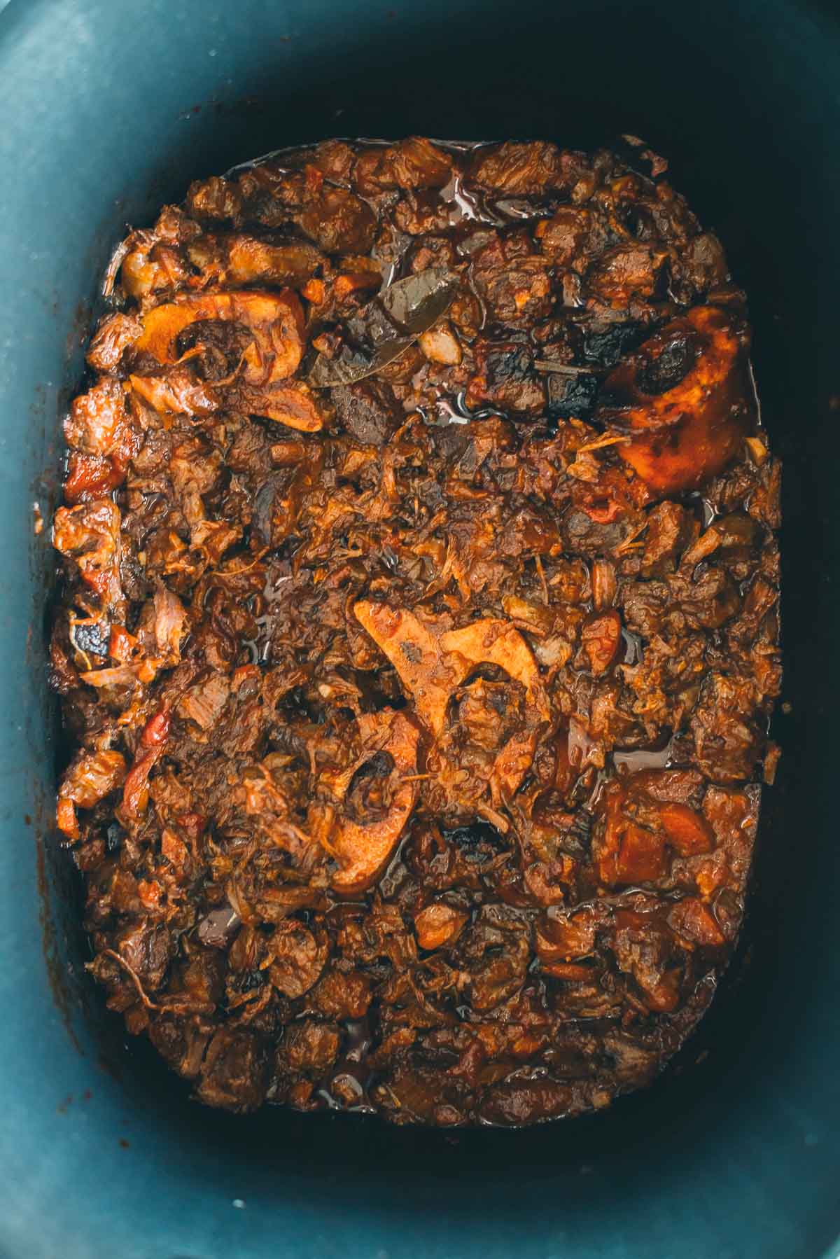 Close-up view of a slow-cooked beef shanks, shredded with visible bones and rich, dark sauce in a pot.