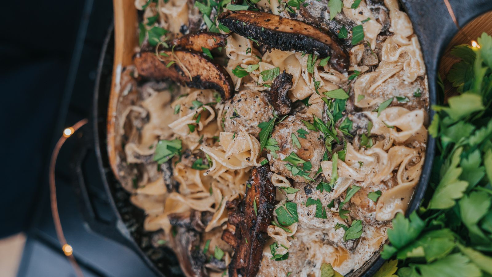 A skillet filled with creamy pasta garnished with herbs and topped with sliced mushrooms.