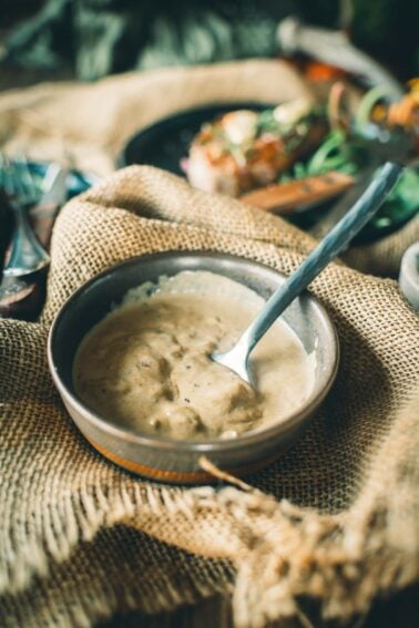 A bowl of mustard cream sauce with a spoon, set on a burlap cloth.