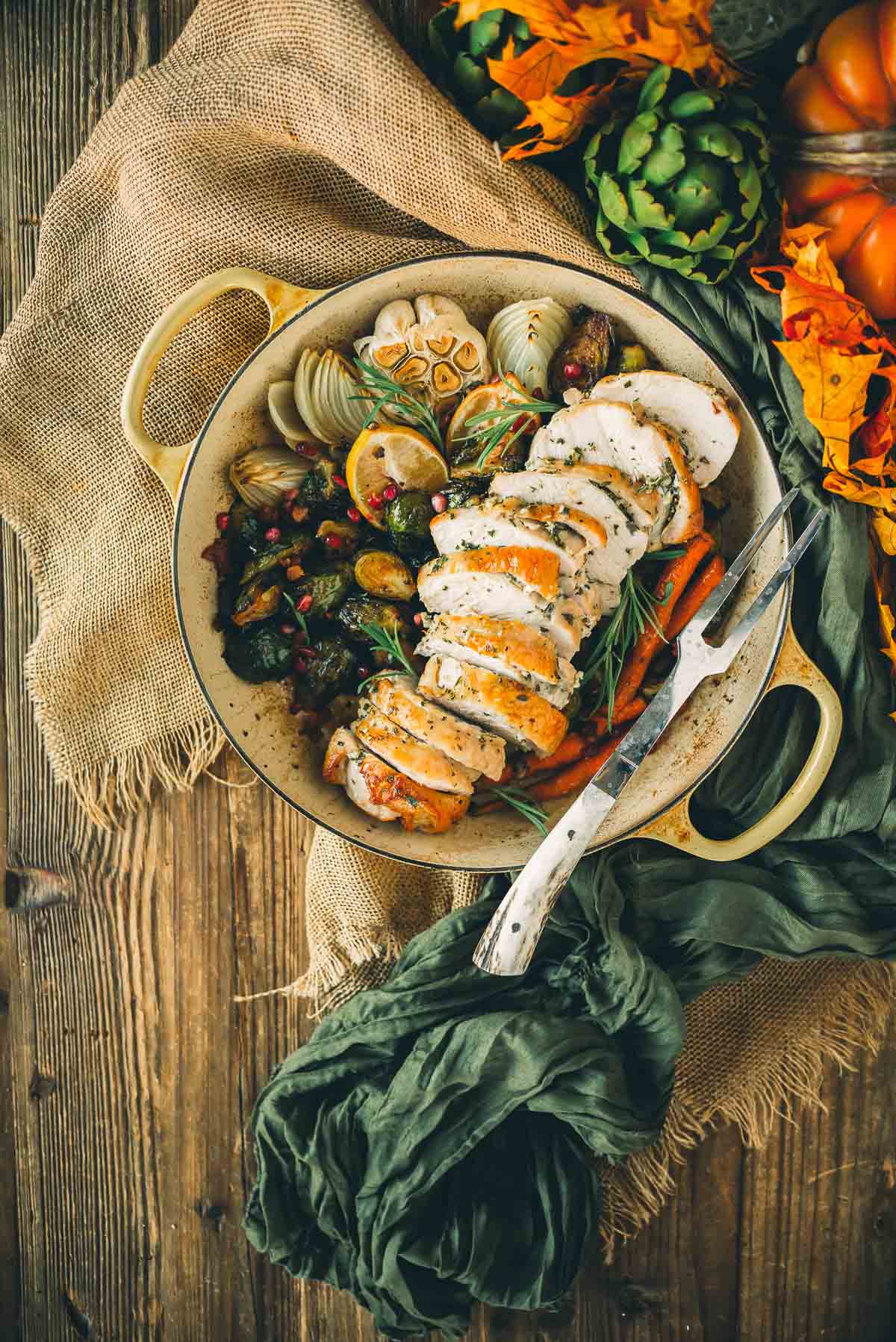 Roasted turkey slices with vegetables, garlic, and herbs in a round dish on a wooden table, surrounded by fall decorations.