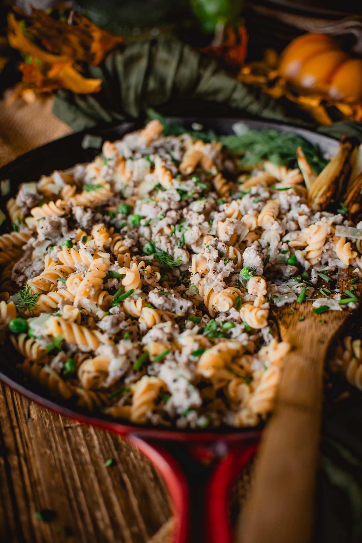 A skillet of ground turkey stroganoff with herbs and a creamy sauce, garnished with finely chopped parsley, is served on a wooden table.