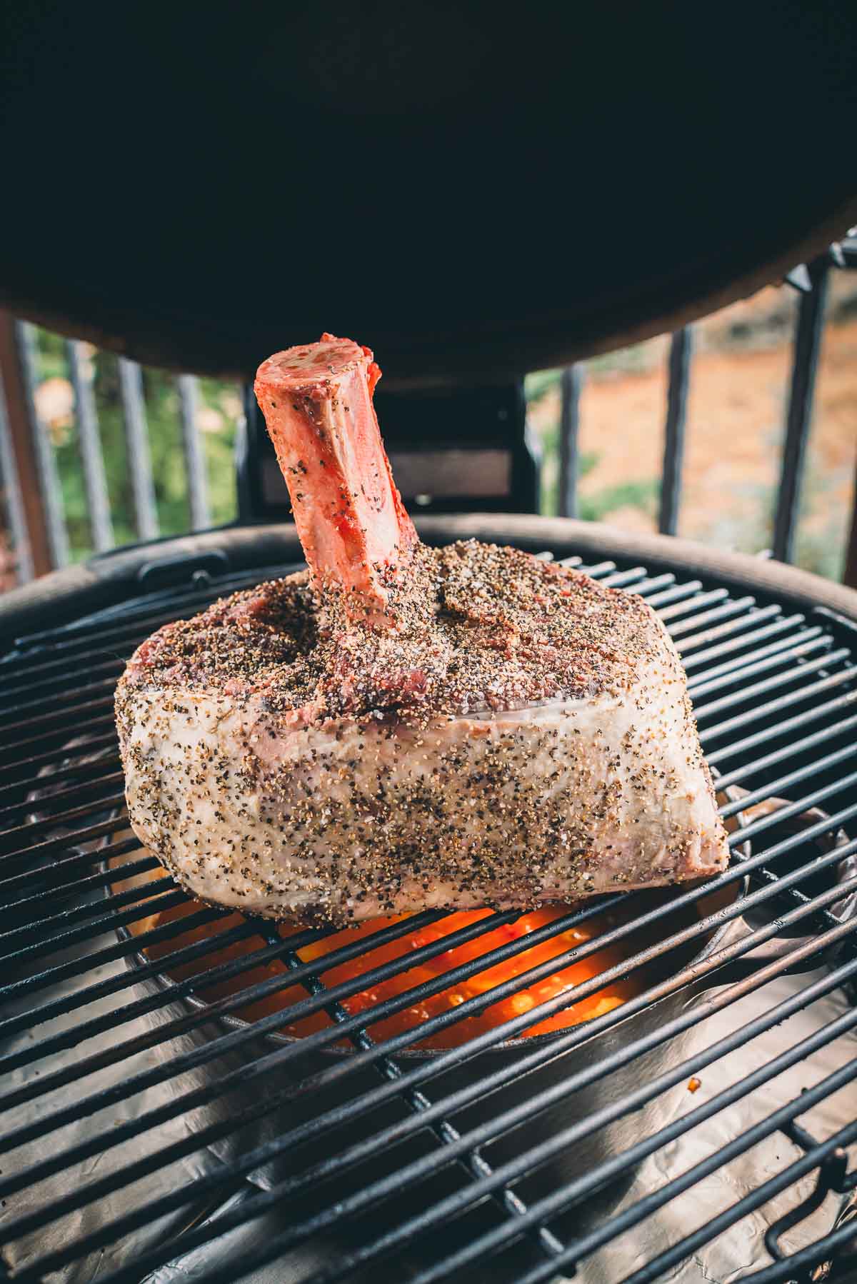 A seasoned beef shank is grilling on an outdoor barbecue with visible flames beneath the grill rack.