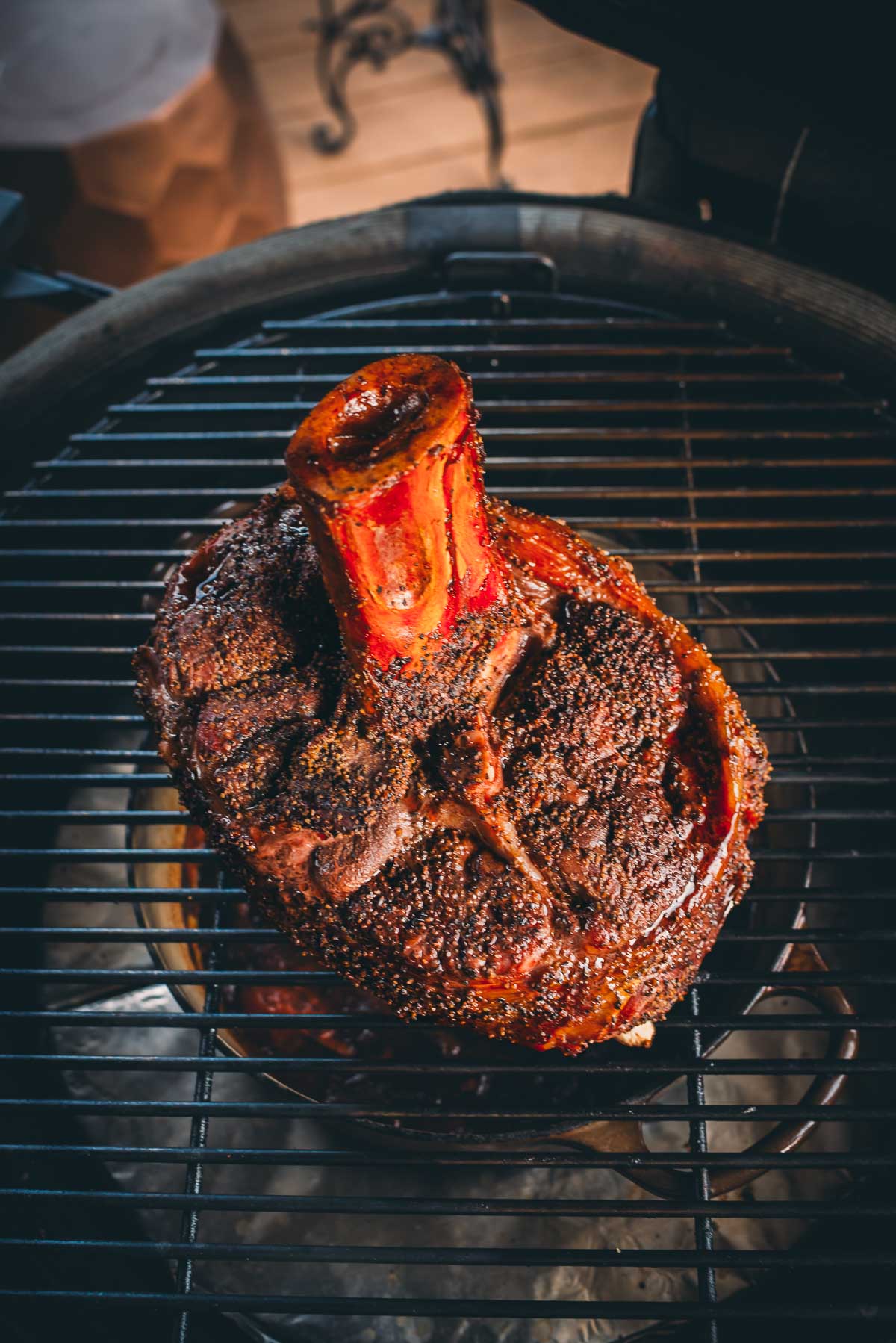 Close-up of a large, seasoned beef shank on the bone, grilling on a barbecue.