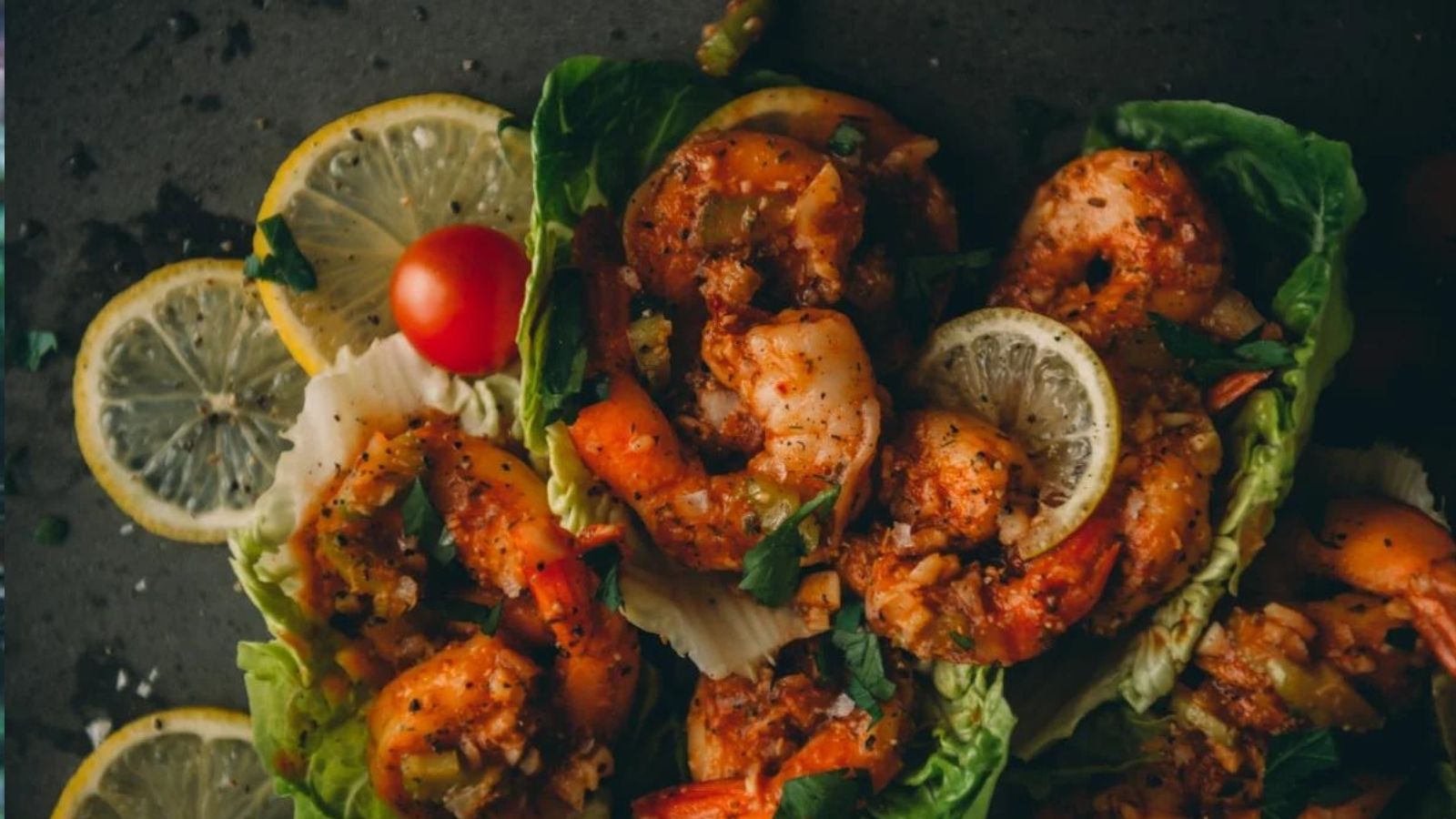 Grilled shrimp on lettuce leaves, garnished with lemon slices, cherry tomatoes, and herbs.