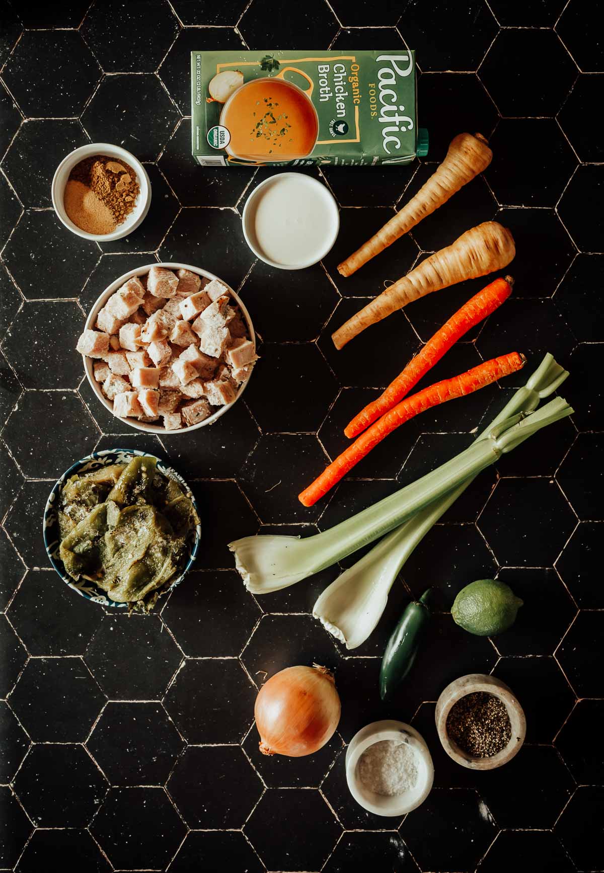 Ingredients on a black tile surface include chicken broth, leftover turkey, parsnips, carrots, celery, diced bread, green chilies, onion, jalapeño, lime, and seasonings in small bowls.