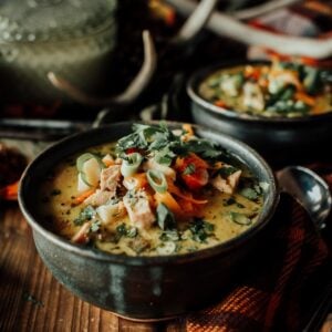 Bowl of creamy turkey soup garnished with sliced green onions and cilantro, set on a wooden table next to a plaid cloth and spoon.