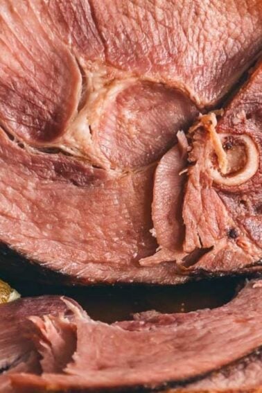 Close-up of a sliced glazed ham garnished with orange slices, fresh herbs, and berries on a wooden platter.