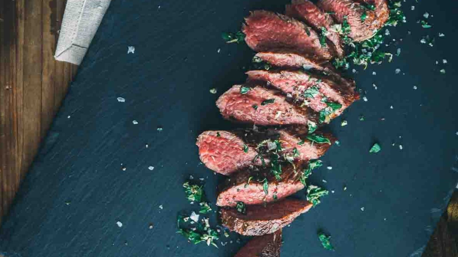 Sliced medium-rare steak garnished with herbs on a slate board.