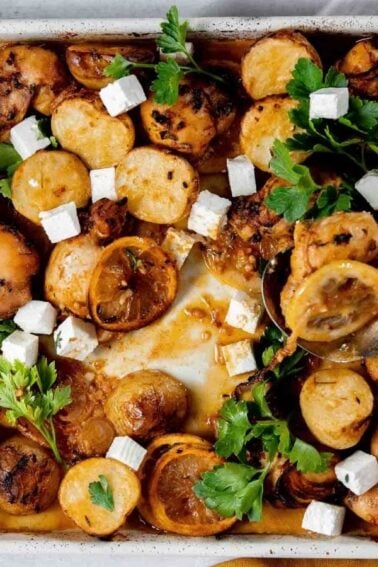 Baked chicken and potatoes in a roasting pan, garnished with fresh herbs and cubed cheese.