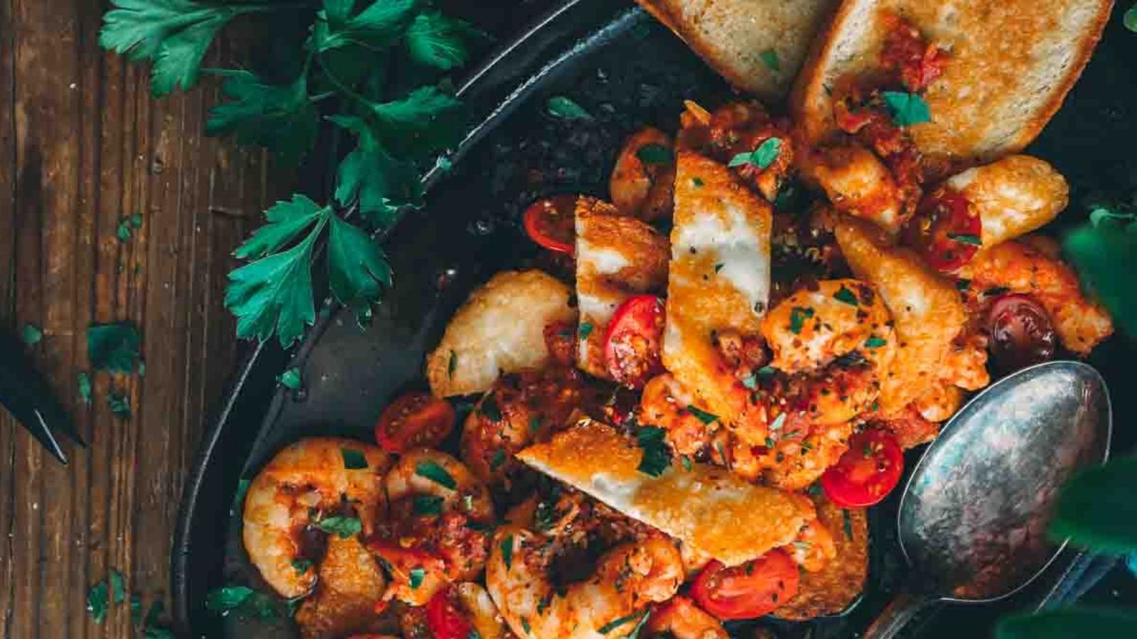 A plate of shrimp, tomatoes, and herbs with toasted bread on the side.