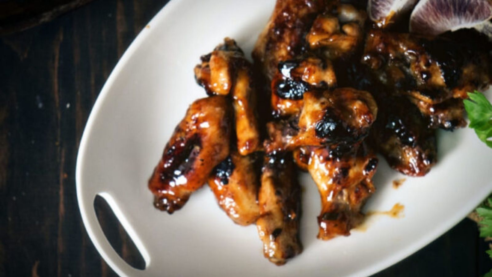 A white plate with grilled chicken wings drizzled in sauce, placed on a dark wooden table.