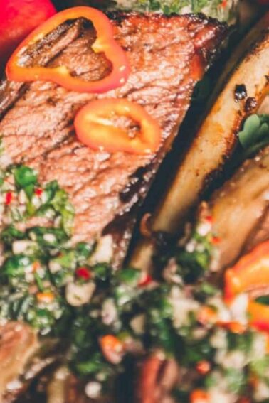 Grilled beef ribs garnished with green herbs and sliced red peppers on a bed of arugula.