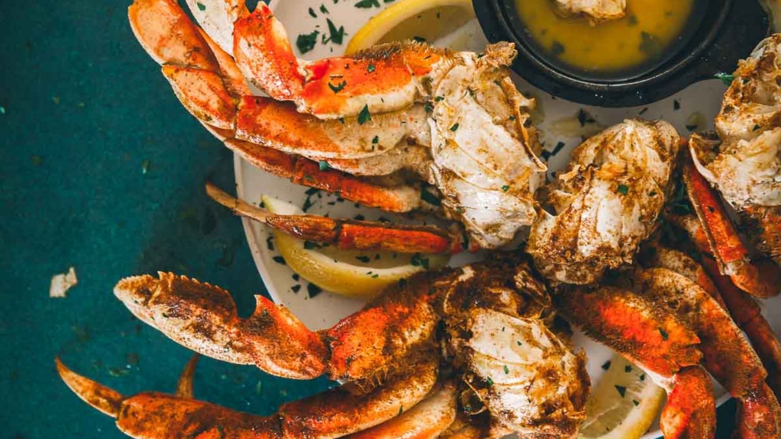 Cooked crab legs served on a plate with lemon wedges and a small bowl of dipping sauce.