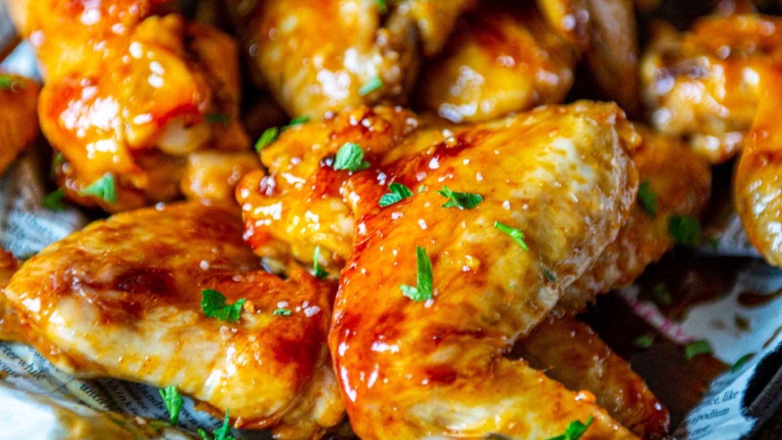 Close-up of golden-brown chicken wings glazed in sauce and garnished with chopped herbs.