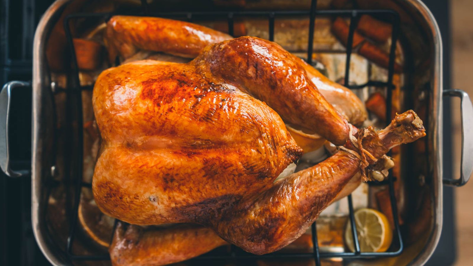 A whole roasted turkey on a rack in a baking pan, with a golden-brown skin. Lemons and vegetables are placed around it.