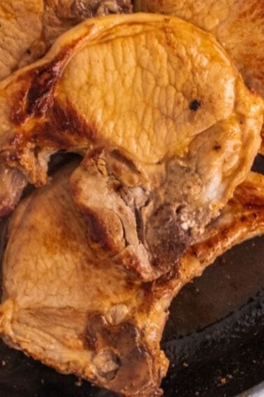 Cooked pork chops in a black skillet on a marble surface.
