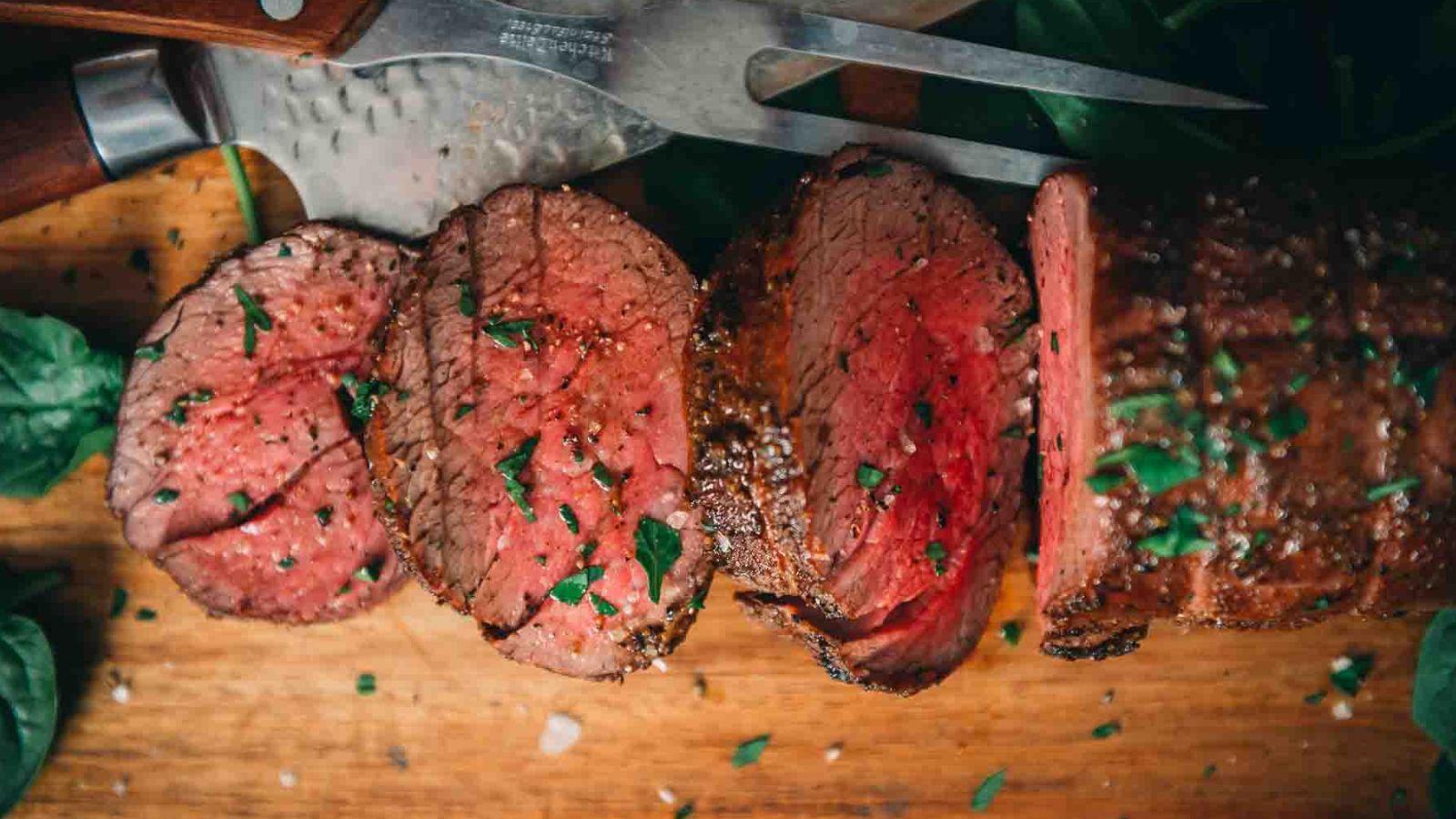 Sliced medium-rare beef tenderloin on a wooden cutting board, garnished with chopped herbs, pairs perfectly with the best sauces for beef tenderloin.