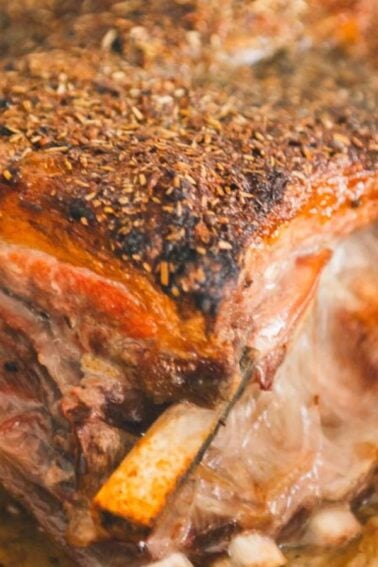 Close-up of a seasoned, roasted rack of ribs with visible herbs and spices, surrounded by lemon wedges and onions.