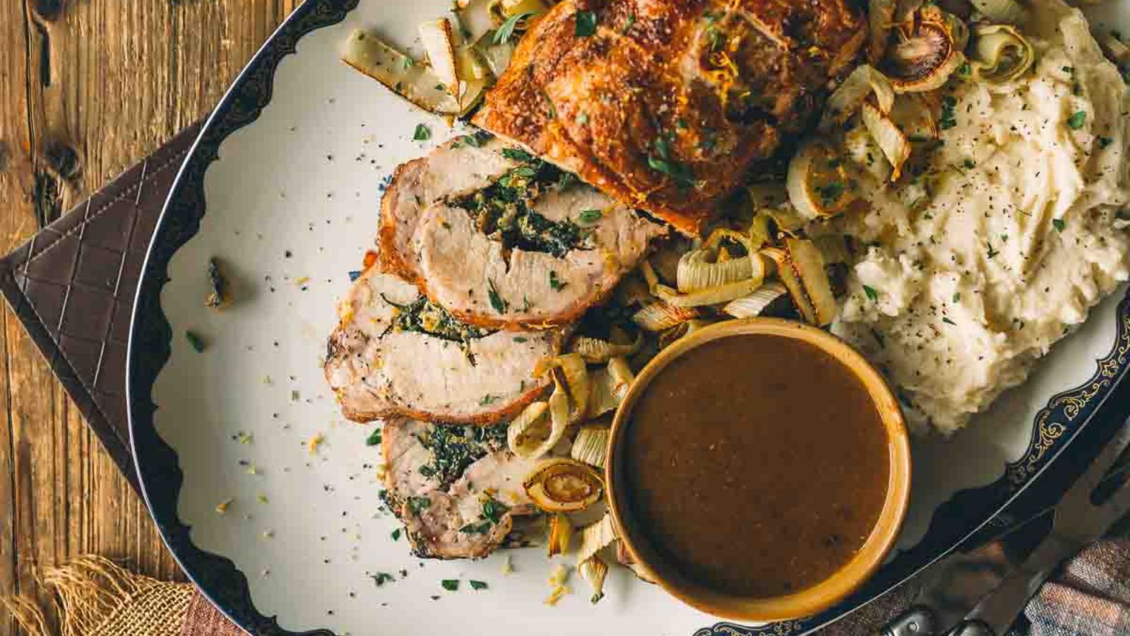 Roast pork with lemon slices, served with mashed potatoes, gravy, and roasted onions on a decorative plate.