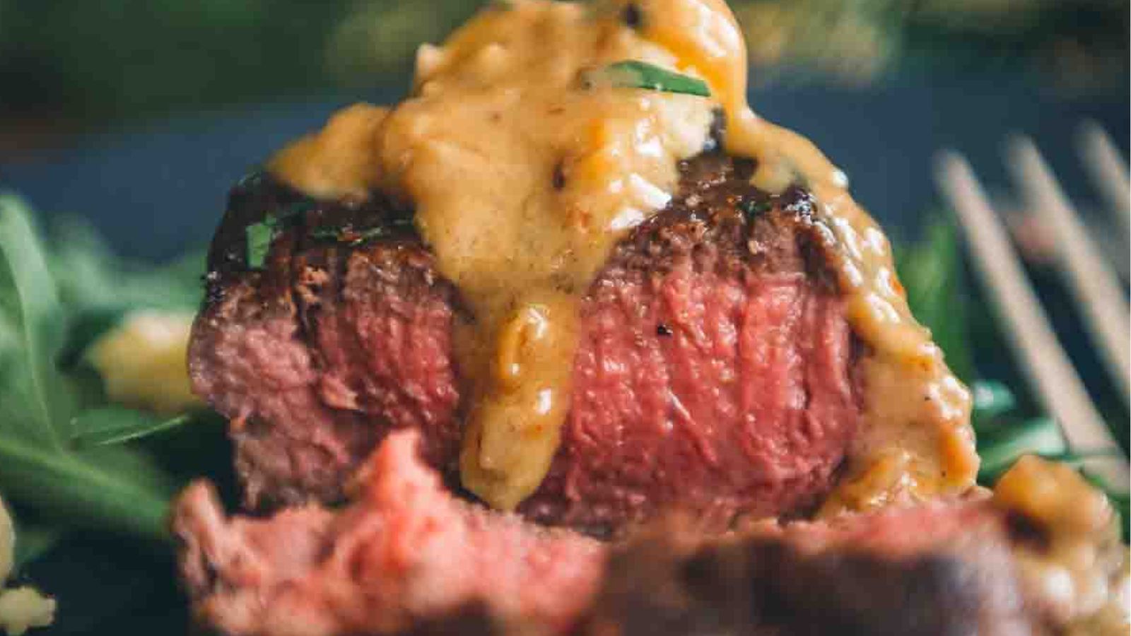 Close-up of a medium-rare steak topped with one of the best sauces for beef tenderloin, a creamy delight, placed on a dark plate with a fork nearby.