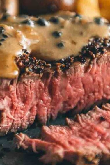 Close-up of a sliced medium-rare steak topped with one of the best sauces for beef tenderloin, a rich peppercorn blend, accompanied by mushrooms and leafy greens.