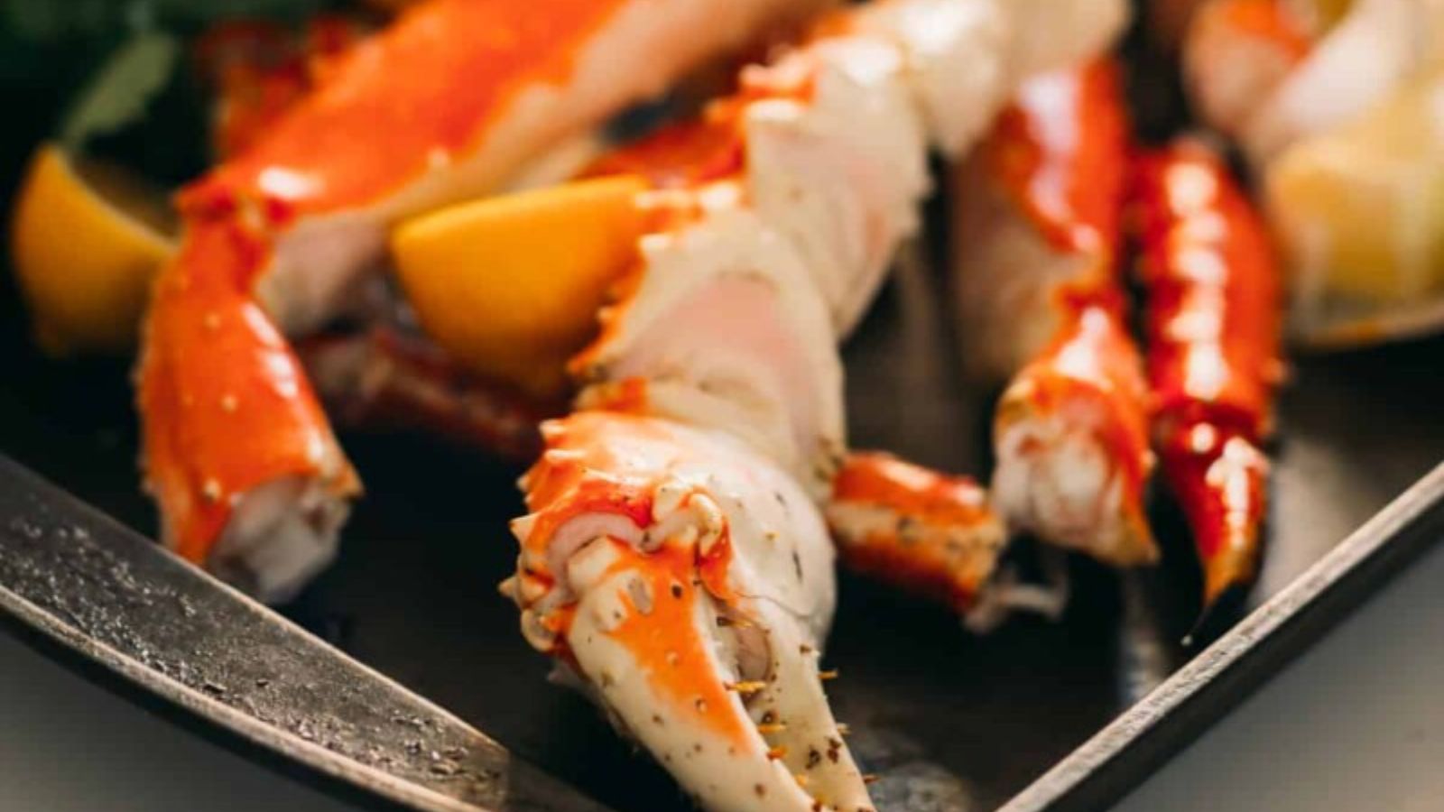 Cooked crab legs and lemon wedges on a metal tray.