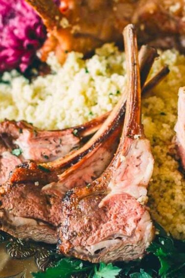 Roasted rack of lamb on a bed of couscous, garnished with fresh herbs and purple flowers on an ornate plate.