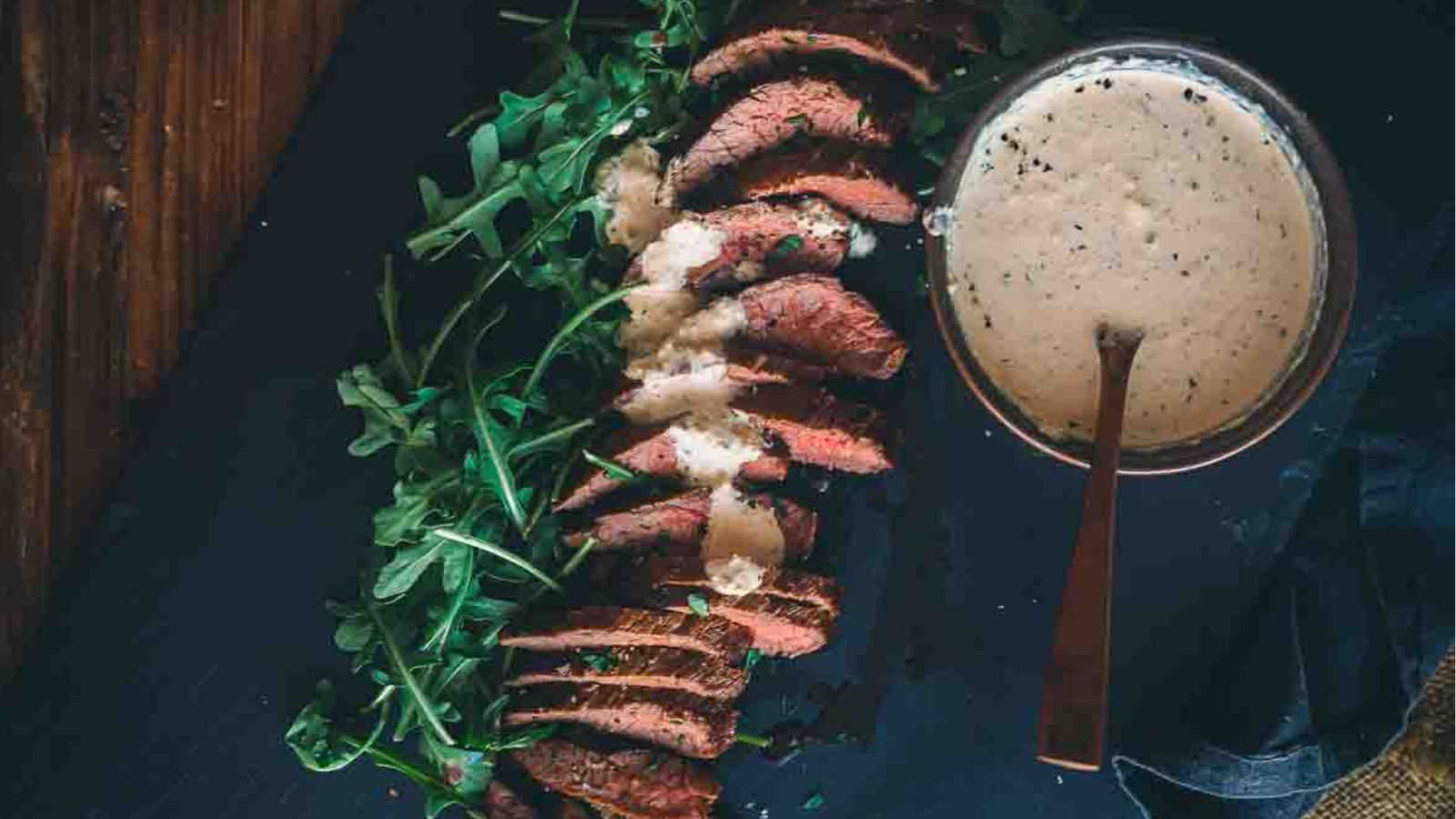 Sliced steak with arugula, accompanied by one of the best sauces for beef tenderloin, elegantly presented on a dark surface.